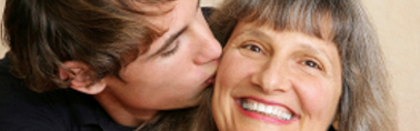 Young adult/late teen son kissing his mother on the cheek.
